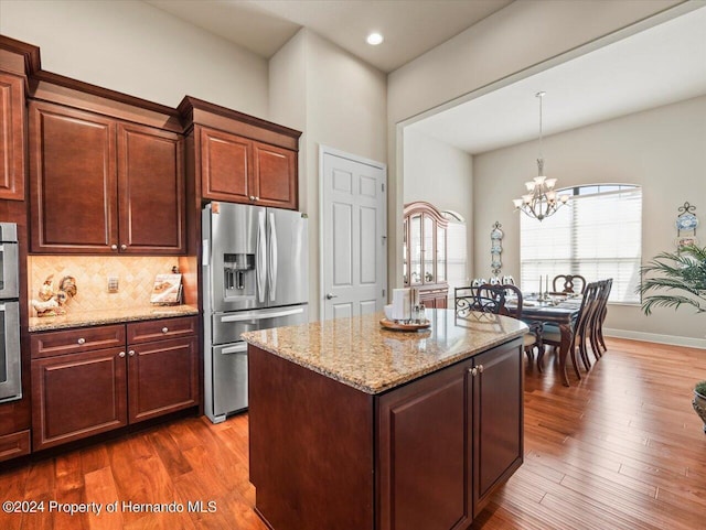 kitchen featuring decorative light fixtures, decorative backsplash, a notable chandelier, a kitchen island, and stainless steel fridge with ice dispenser