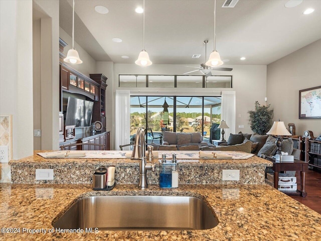 kitchen with light stone countertops, ceiling fan, hanging light fixtures, and sink