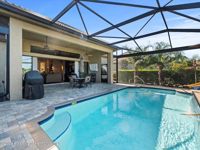 view of swimming pool with ceiling fan, a patio area, and glass enclosure