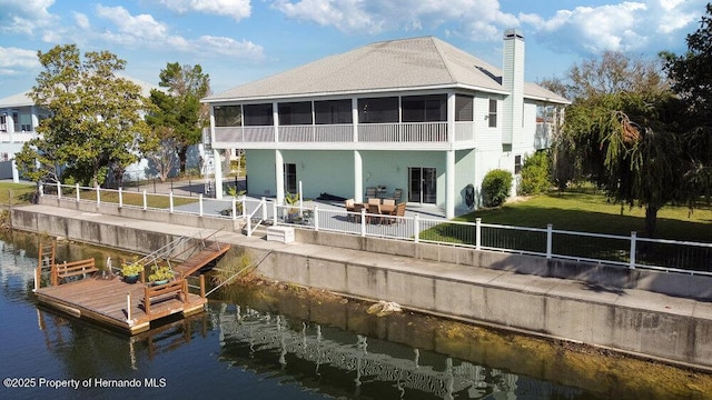 rear view of house featuring a lawn, a patio area, a sunroom, and a water view