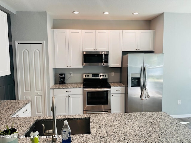 kitchen featuring light stone counters, white cabinetry, sink, and appliances with stainless steel finishes