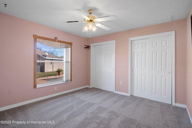 unfurnished bedroom with carpet floors, ceiling fan, and multiple closets