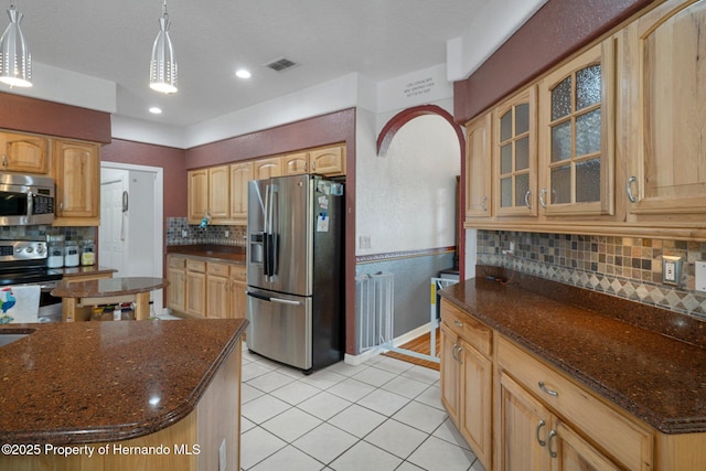 kitchen with decorative light fixtures, appliances with stainless steel finishes, dark stone countertops, and decorative backsplash