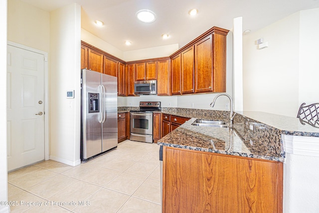 kitchen featuring a sink, dark stone counters, appliances with stainless steel finishes, brown cabinetry, and light tile patterned floors