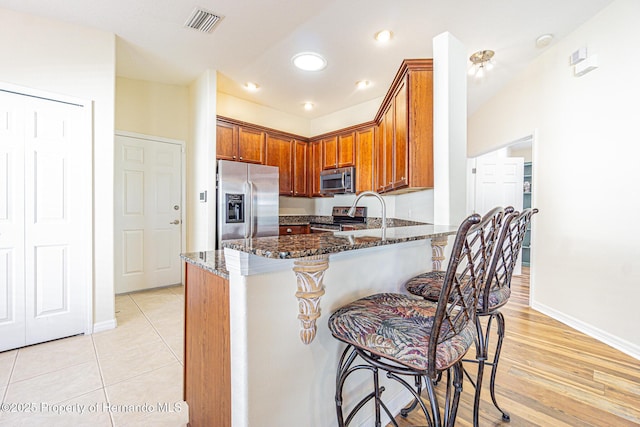 kitchen with a breakfast bar area, visible vents, dark stone counters, a peninsula, and stainless steel appliances