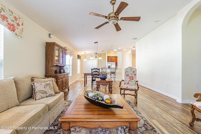 living area with lofted ceiling, a ceiling fan, wood finished floors, arched walkways, and baseboards