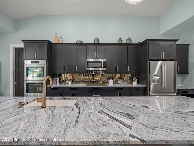 kitchen with tasteful backsplash, light stone counters, vaulted ceiling, and appliances with stainless steel finishes