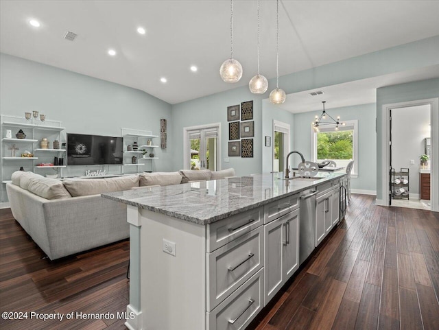 kitchen with stainless steel dishwasher, decorative light fixtures, light stone counters, and a kitchen island with sink