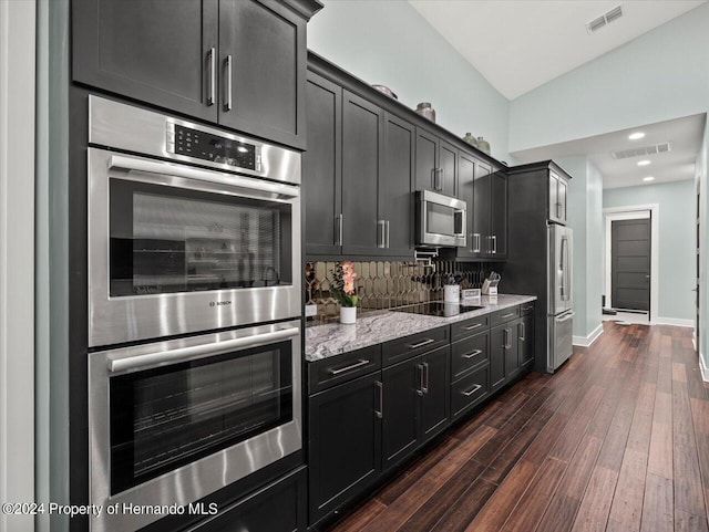 kitchen with dark wood-type flooring, tasteful backsplash, light stone counters, vaulted ceiling, and appliances with stainless steel finishes