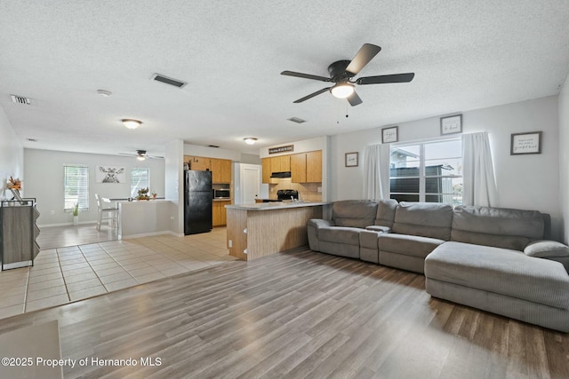 living room with a textured ceiling, light wood-type flooring, and ceiling fan