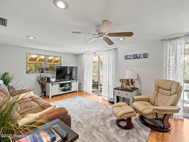 living room with a textured ceiling, light hardwood / wood-style floors, and ceiling fan