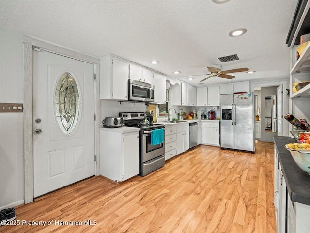 kitchen with a textured ceiling, stainless steel appliances, sink, light hardwood / wood-style flooring, and white cabinetry