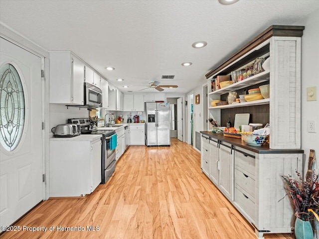 kitchen with a textured ceiling, light wood-type flooring, white cabinetry, and stainless steel appliances