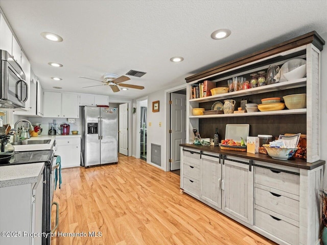 kitchen featuring appliances with stainless steel finishes, a textured ceiling, ceiling fan, light hardwood / wood-style flooring, and white cabinets