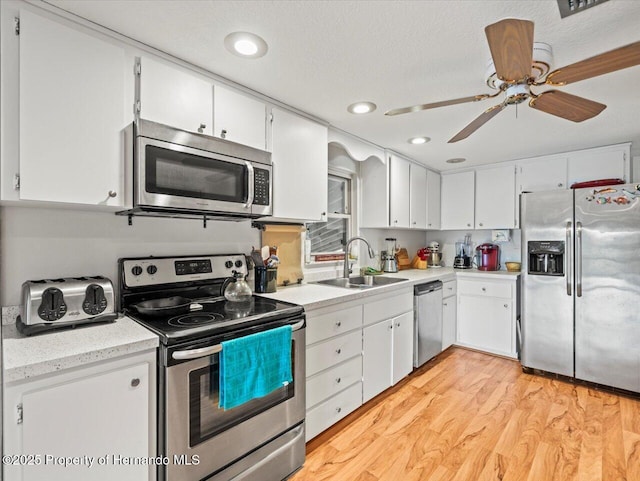 kitchen with white cabinetry, sink, light hardwood / wood-style floors, a textured ceiling, and appliances with stainless steel finishes