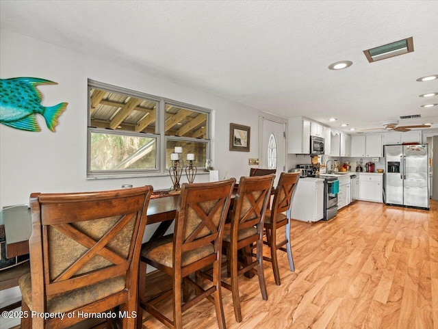 dining area with ceiling fan, sink, light wood-type flooring, and a textured ceiling