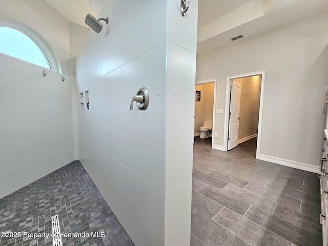 bathroom featuring a tile shower, crown molding, a tray ceiling, and toilet