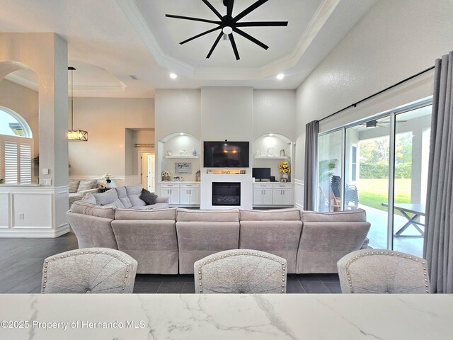 living room with a raised ceiling, ceiling fan, and ornamental molding