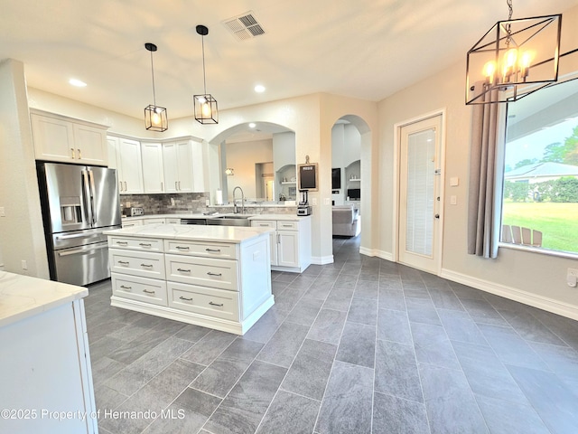 kitchen with sink, hanging light fixtures, stainless steel fridge with ice dispenser, tasteful backsplash, and white cabinetry