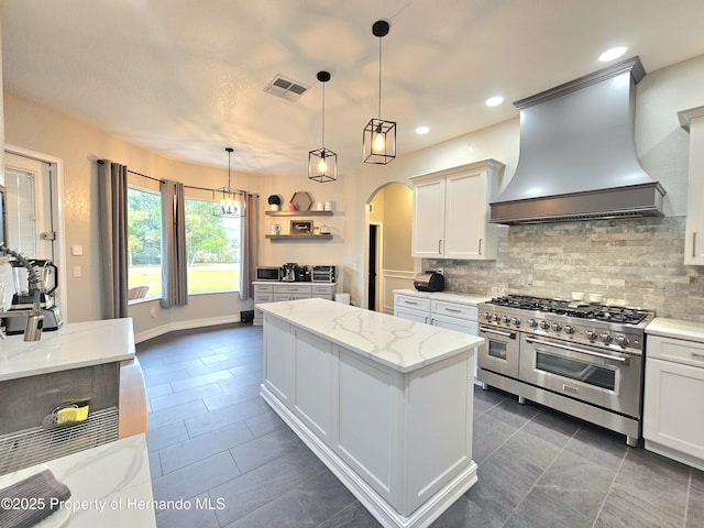 kitchen with white cabinets, a center island, premium range hood, and double oven range