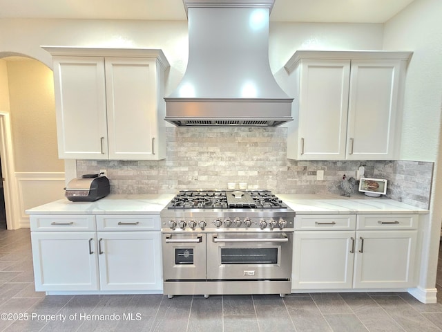 kitchen with white cabinets, backsplash, range with two ovens, and custom exhaust hood