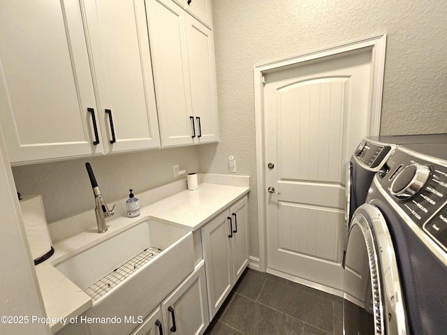 washroom with cabinets, dark tile patterned floors, washer and dryer, and sink