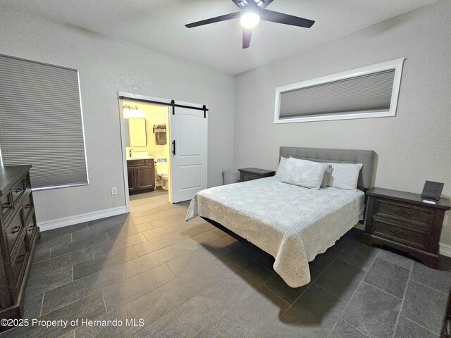 bedroom with a barn door, ensuite bath, and ceiling fan