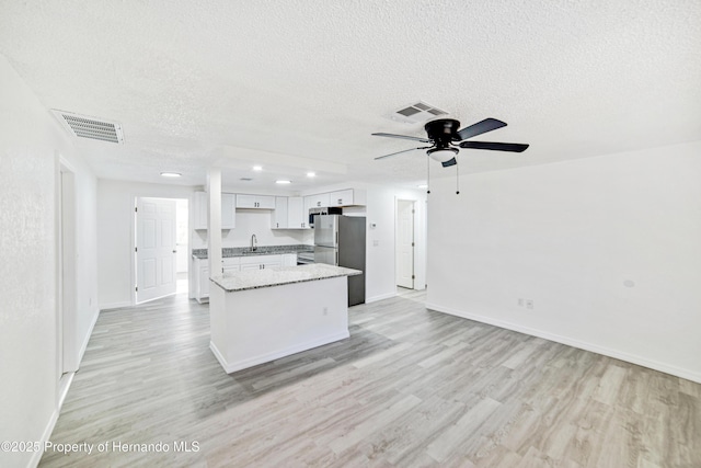 kitchen with light wood-type flooring, a textured ceiling, sink, white cabinets, and stainless steel refrigerator