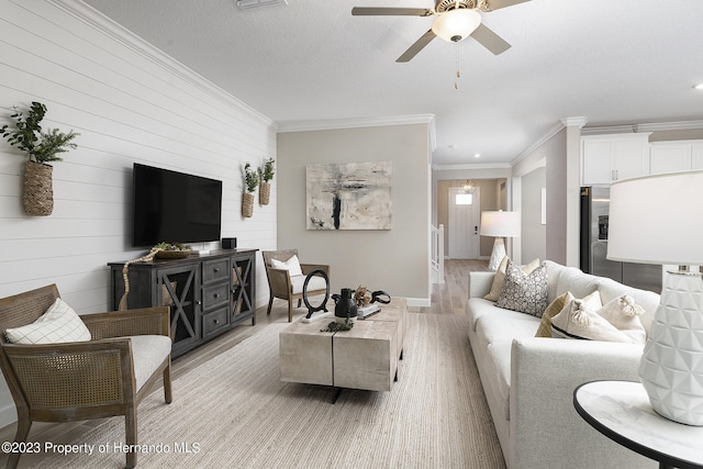 living room with crown molding, wooden walls, ceiling fan, a textured ceiling, and light hardwood / wood-style floors