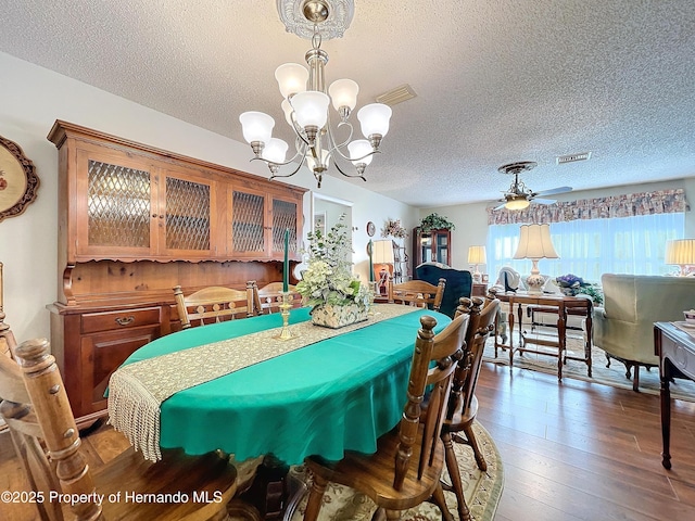 dining room with ceiling fan with notable chandelier, dark wood-type flooring, and a textured ceiling