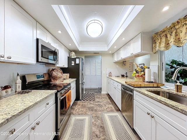 kitchen with sink, white cabinetry, a raised ceiling, light stone countertops, and appliances with stainless steel finishes