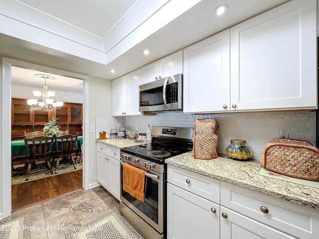 kitchen featuring light stone counters, stainless steel appliances, an inviting chandelier, backsplash, and white cabinets