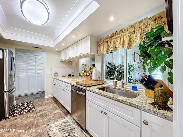 kitchen with appliances with stainless steel finishes, light stone counters, a tray ceiling, sink, and white cabinetry