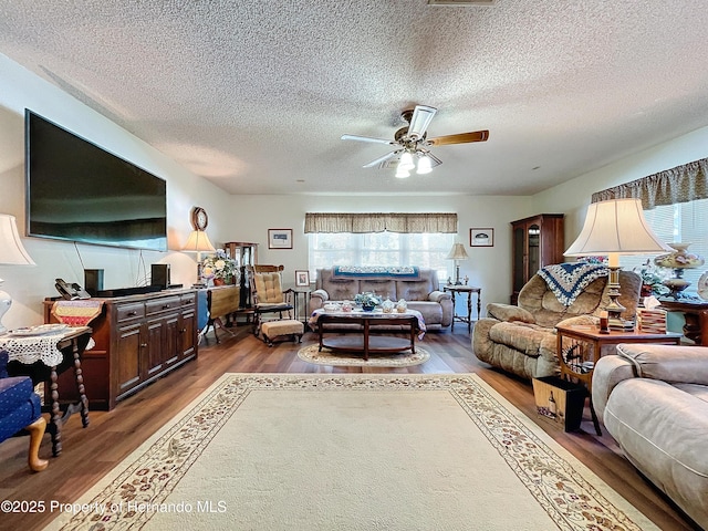 living room with a textured ceiling, ceiling fan, and dark hardwood / wood-style floors