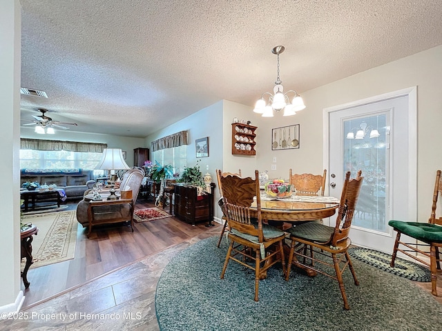 dining room with ceiling fan with notable chandelier, a textured ceiling, and wood-type flooring