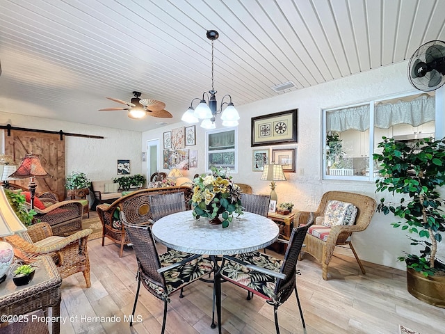 dining room featuring light wood-type flooring, a barn door, and ceiling fan with notable chandelier