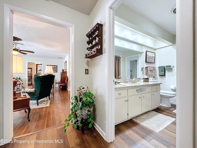 interior space with toilet, hardwood / wood-style flooring, a textured ceiling, ceiling fan, and vanity