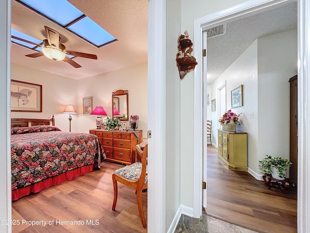 bedroom with ceiling fan, light hardwood / wood-style flooring, a skylight, and a textured ceiling