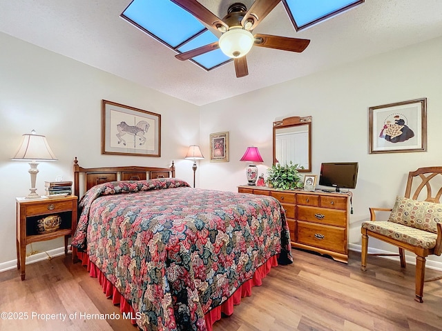 bedroom with ceiling fan, a skylight, and light wood-type flooring