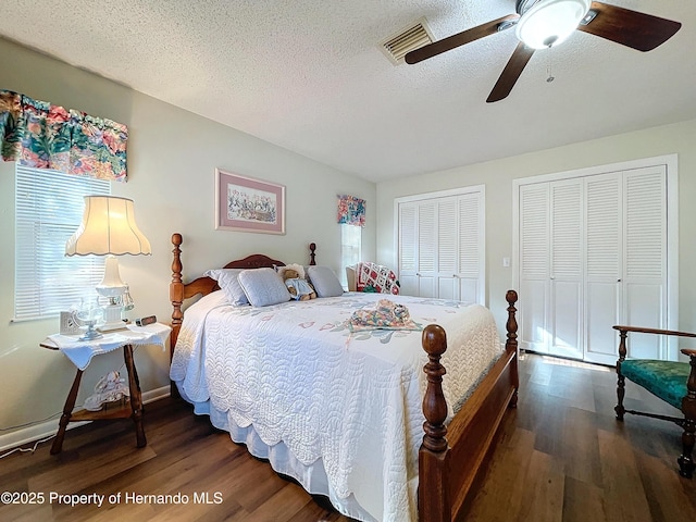 bedroom featuring ceiling fan, dark wood-type flooring, two closets, and a textured ceiling