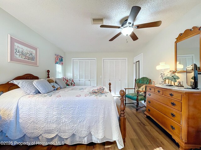 bedroom featuring ceiling fan, hardwood / wood-style floors, two closets, and a textured ceiling