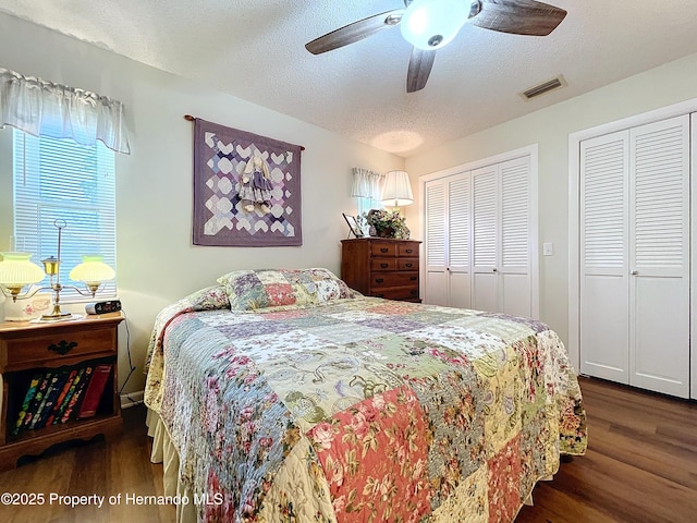 bedroom featuring ceiling fan, two closets, a textured ceiling, and dark hardwood / wood-style floors