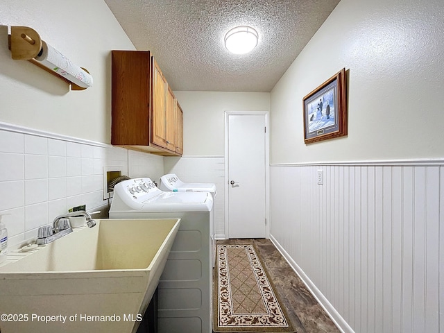 clothes washing area featuring a textured ceiling, cabinets, sink, and washing machine and clothes dryer