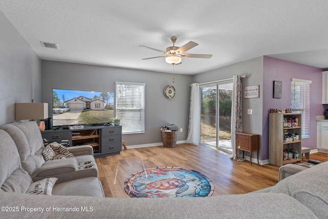 living room with ceiling fan, light wood-type flooring, and a textured ceiling