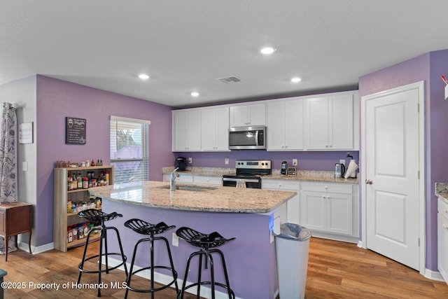 kitchen with sink, stainless steel appliances, an island with sink, light hardwood / wood-style floors, and white cabinets