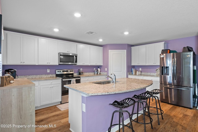 kitchen featuring white cabinetry, sink, stainless steel appliances, an island with sink, and wood-type flooring