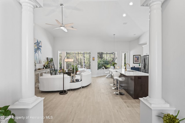 living room with ceiling fan, sink, a high ceiling, and light hardwood / wood-style flooring