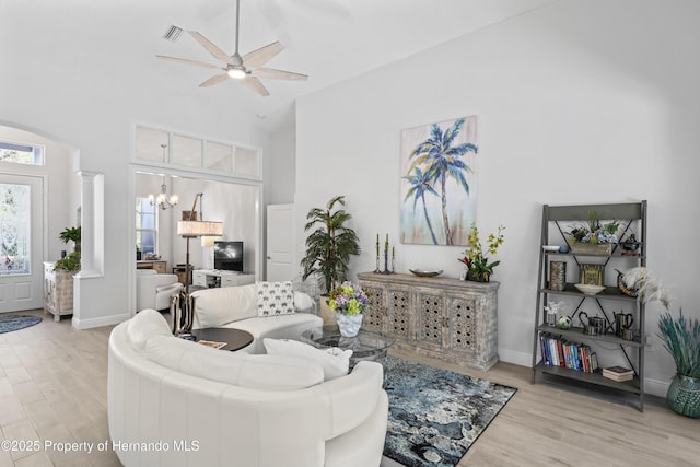 living room featuring ceiling fan with notable chandelier, light hardwood / wood-style flooring, high vaulted ceiling, and decorative columns