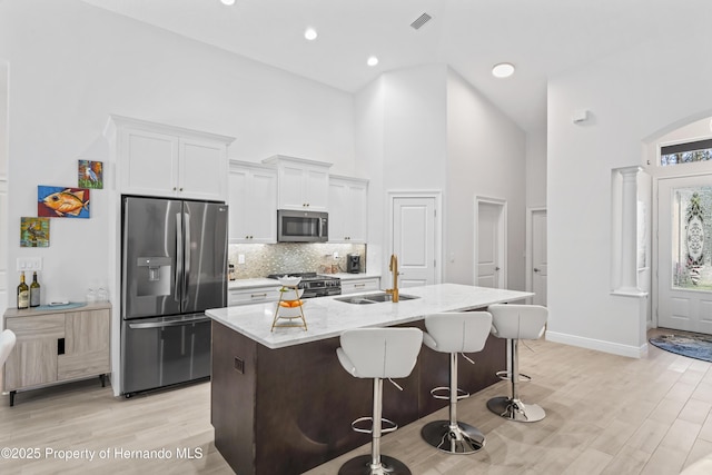 kitchen with stainless steel appliances, a kitchen island with sink, sink, white cabinets, and a high ceiling