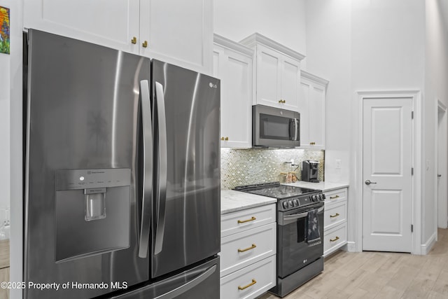 kitchen featuring backsplash, light hardwood / wood-style flooring, light stone countertops, white cabinetry, and stainless steel appliances